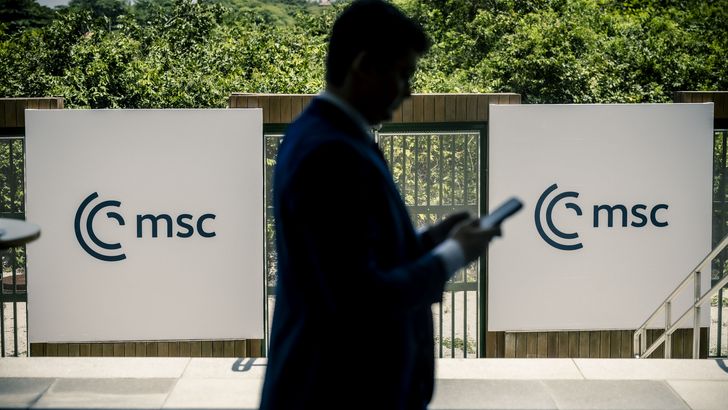 Man walking in front of MSC logo with cell phone in hand.